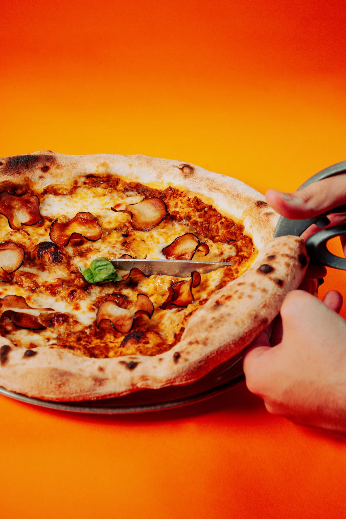 Pizza appena sfornata, tagliata con le forbici, su fondo arancione