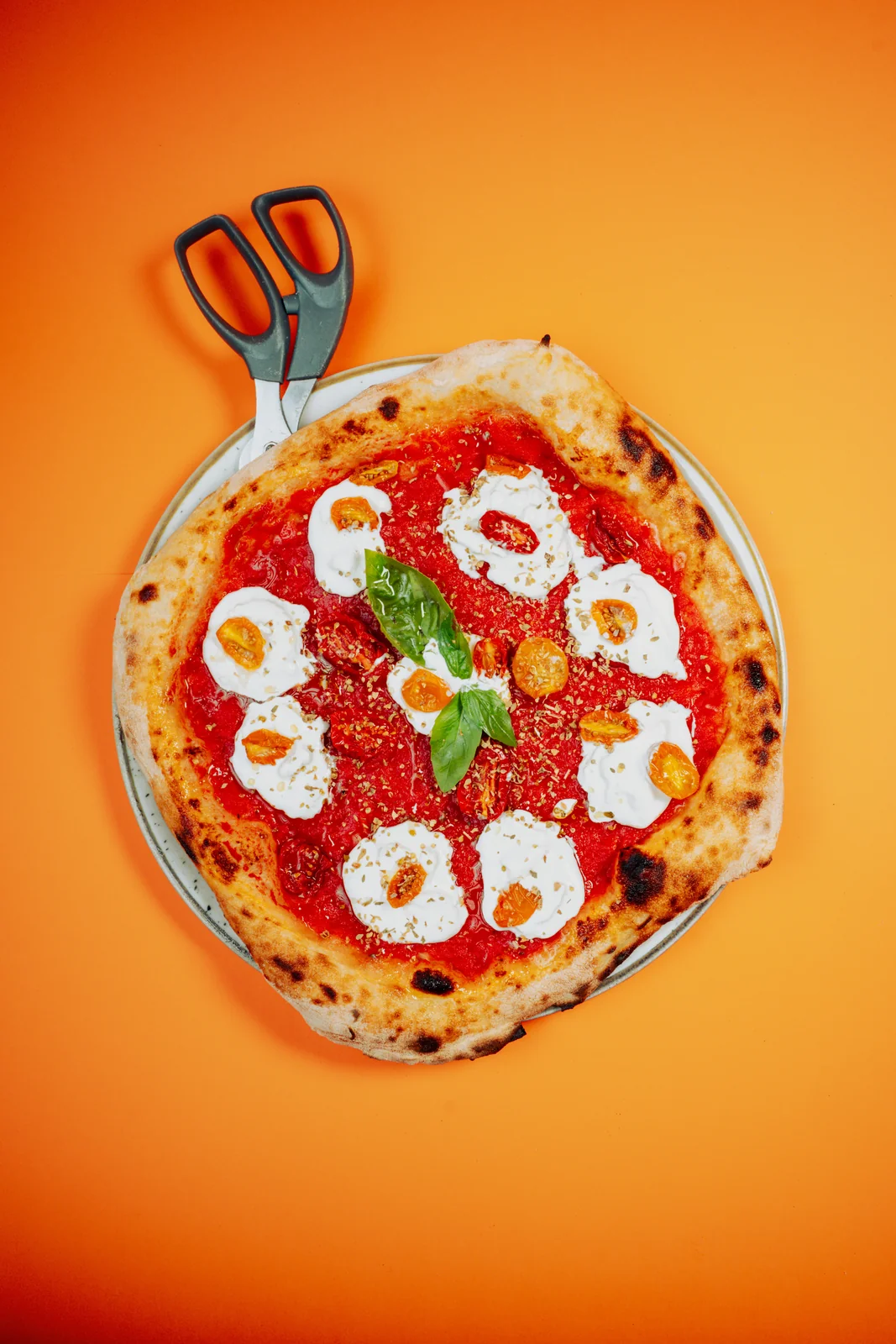 Pizza su fondo arancione con pomodoro, basilico e crema bianca